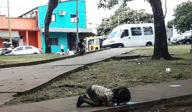 口渴的小女孩跪在地上喝脏水